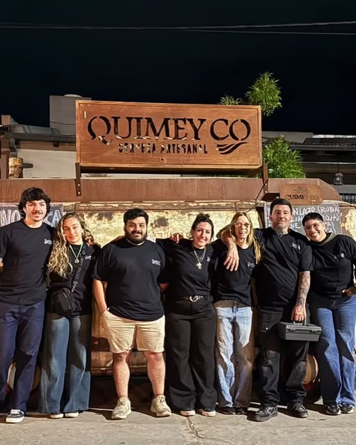 El equipo de Quimey Co, siete personas con remera negra, frente al cartel del local.